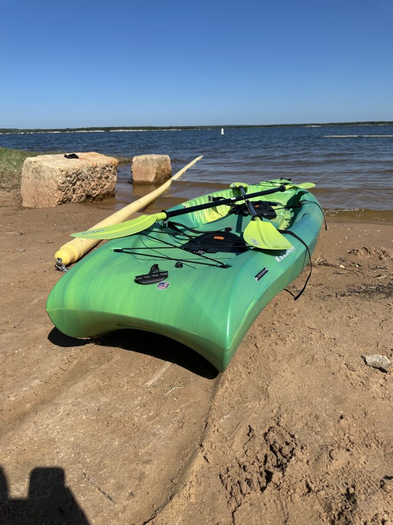 green kayak with paddles on shore