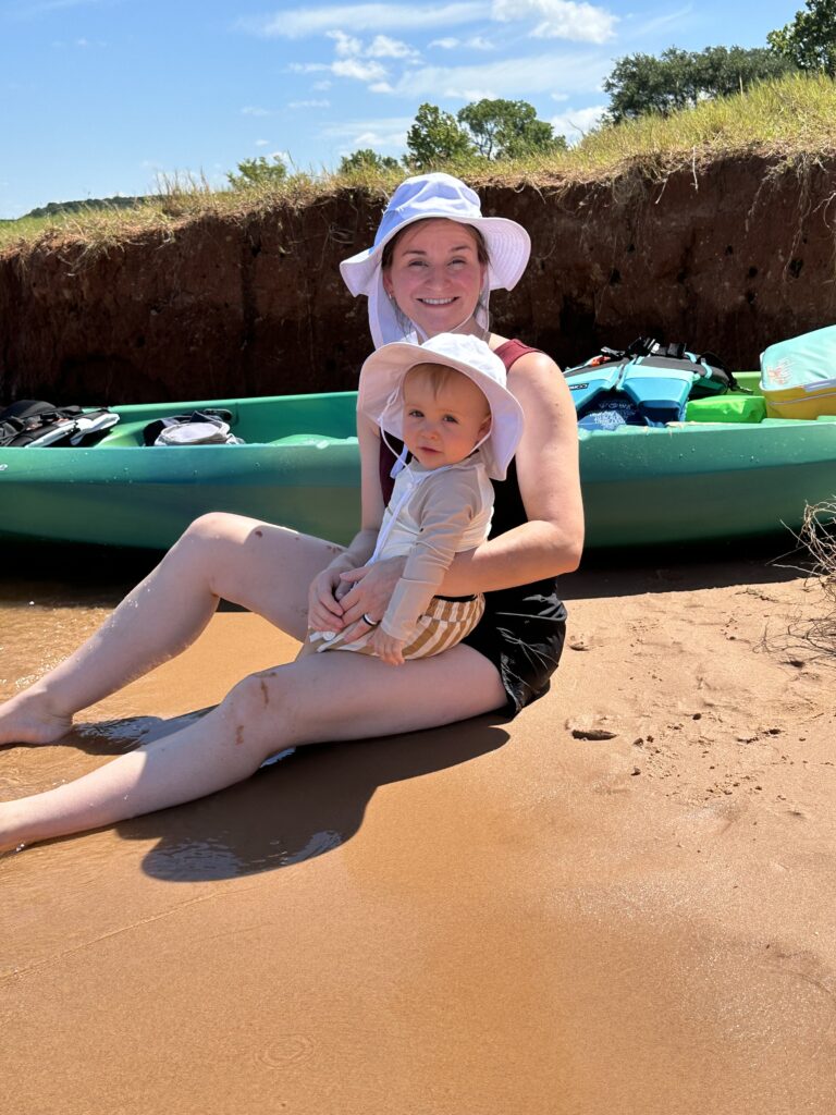 mom and son sitting on lake shore next to green kayak
